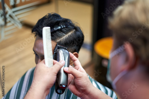 Hands of a baber using an electric razor to cut the hair of a client