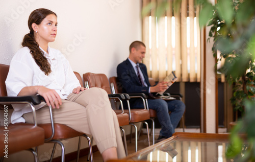 Concentrated young girl sits in a chair in the lobby of a business center, waiting for her turn to see a specialist