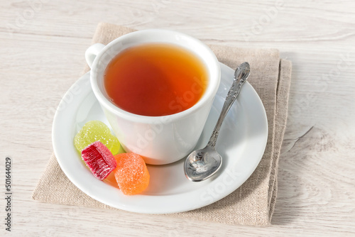 A cup of hot tea with jelly fruit marmalade on a linen napkin.