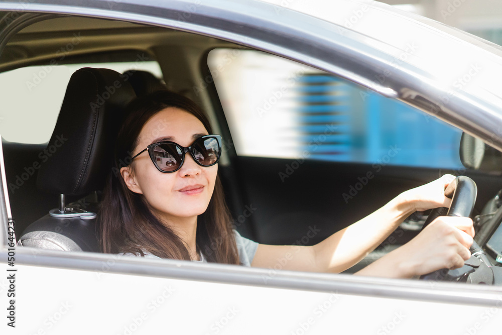 Happy asian woman driving a eco hybrid car.Happy woman is driving a car service.Portrait female driver steering car with safety belt.Electric vehicle.used car rental.Learning to drive.vacation travel.