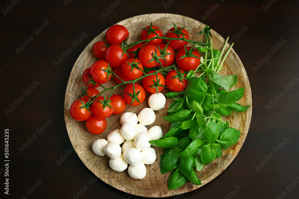 A set of products for caprese salad. Tomatoes, basil and mozzarella on a wooden board. A set of products for caprese salad. Tomatoes, basil and mozzarella on a wooden board.