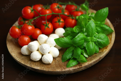 A set of products for caprese salad. Tomatoes, basil and mozzarella on a wooden board.