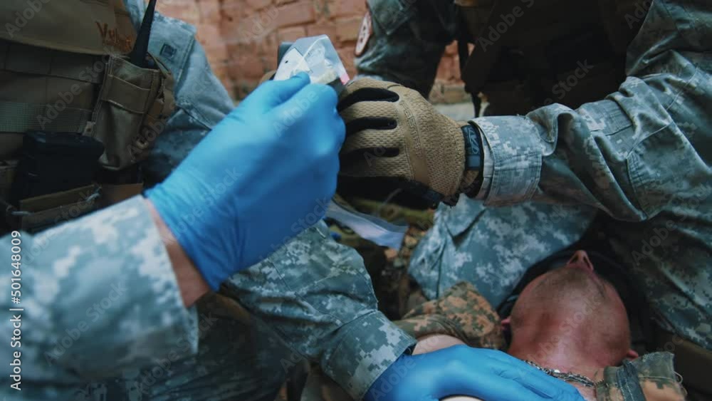 In forest two medics fixed the bandage with adhesive tape, provides first aid. Soldier lying wounded with punctured lungs. Military concept In forest two medics fixed the bandage with adhesive tape, provides first aid. Soldier lying wounded with punctured lungs. Military concept