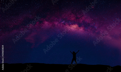 A person standing happily beside the Milky Way Galaxy pointing to a bright star.