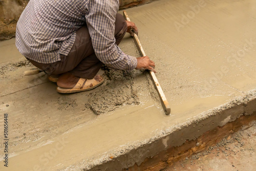 Indian construction worker levelling a cemented floor using wooden leveller manually, Stock image. photo