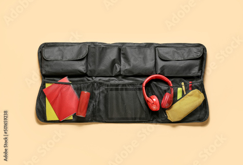 Travel organizer with stationery, headphones and bottle of drink on color background