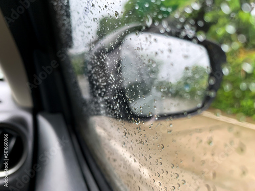Car side glass view in raining with rain drops on it. Bokeh on rear view mirror  car moving amid rain concept.