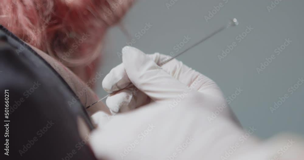 A tattooist's hand holds a needle and tattoos a woman's back using the old handpoke tattoo technique