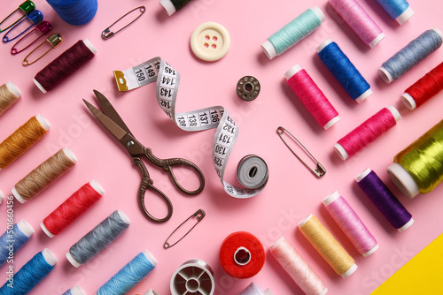 Thread spools, scissors, measuring tape and buttons on pink background