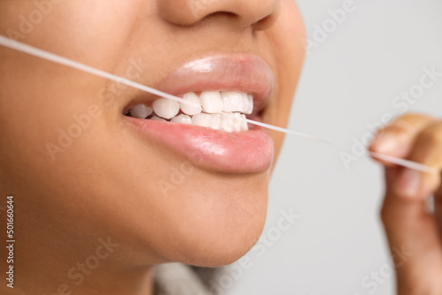 African-American teenage girl flossing teeth on light background, closeup