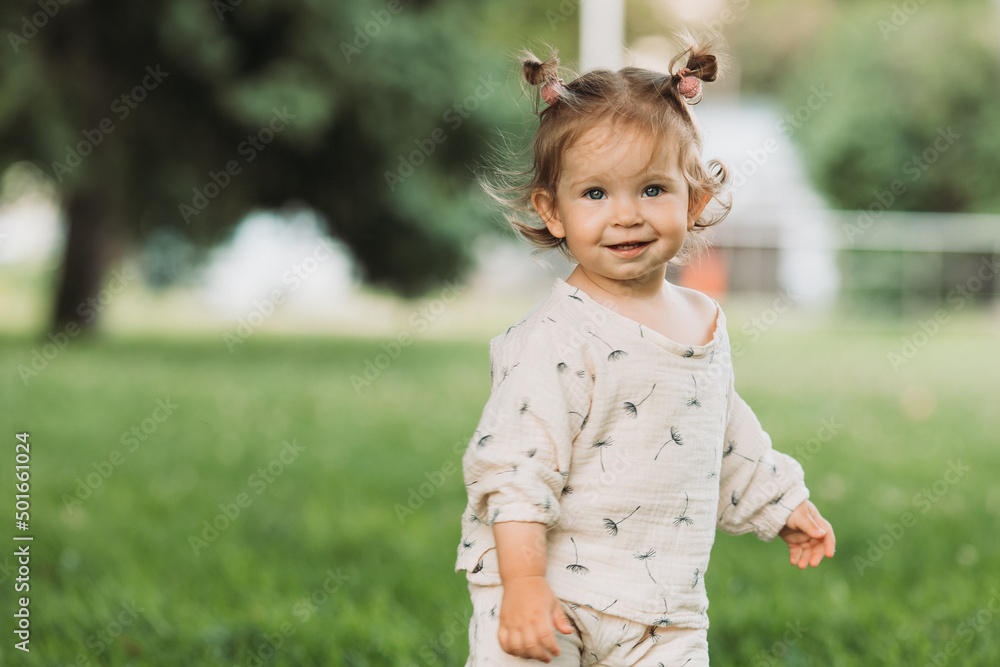 cute little smiling girl with a funny hairstyle hides behind trees and runs and plays in the park cute little smiling girl with a funny hairstyle hides behind trees and runs and plays in the park