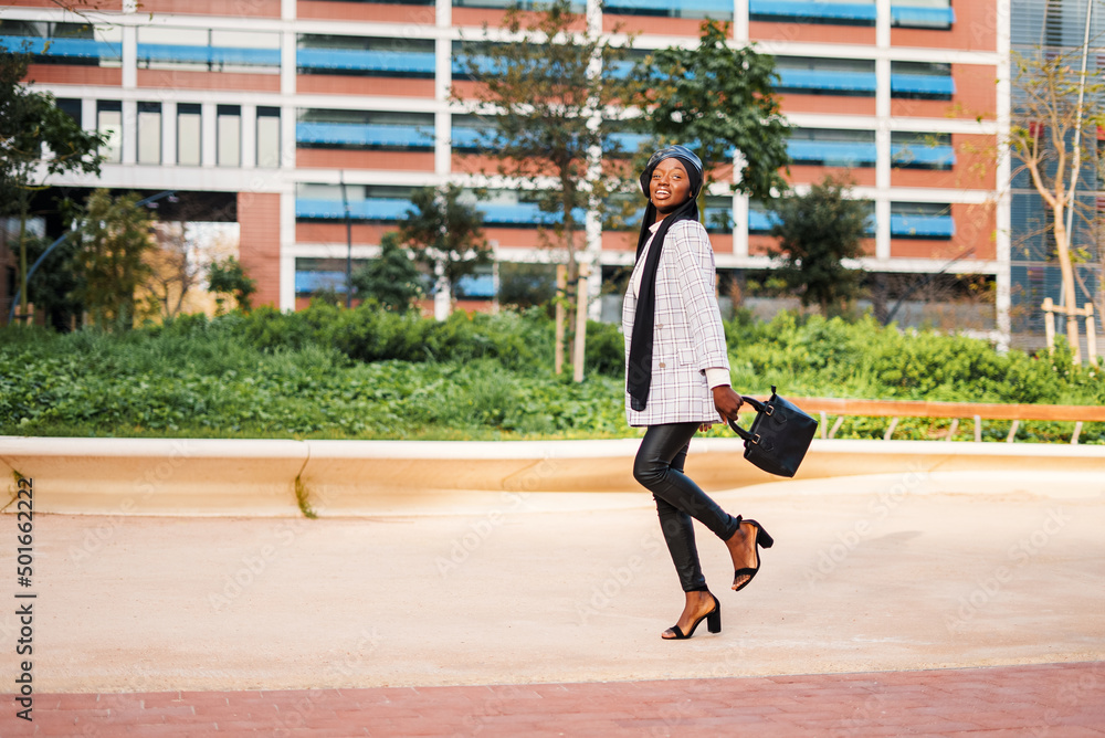 Content black woman in stylish wear walking in park