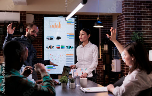 Photos Woman raising hand to ask a question in late night business meeting with sales department in startup office