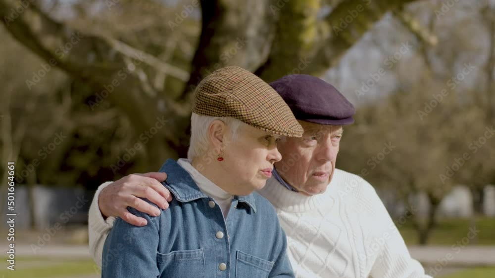 Caucasian elderly couple spending time in park on sunny autumn day. Senior lady and her husband talking and kissing while sitting on bench and discussing something. Retirement, relationship concept Caucasian elderly couple spending time in park on sunny autumn day. Senior lady and her husband talking and kissing while sitting on bench and discussing something. Retirement, relationship concept