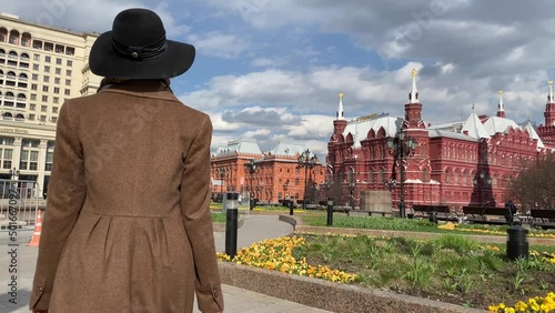 Young beautiful lady elegance madame in hat and coat walking on Red Square  near Historical Museum, Kremlin, Alexander Garden and Okhotny Ryad. Spring, blooming flowers. Center of Moscow, Russia. photo