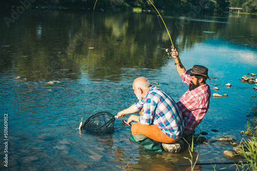 Two men friends fishing. Flyfishing angler makes cast, standing in river water. Old and young fisherman. Catching trout fish.