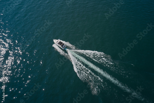 Yacht in the rays of the sun on blue water. Top view of a white boat sailing to the blue sea.