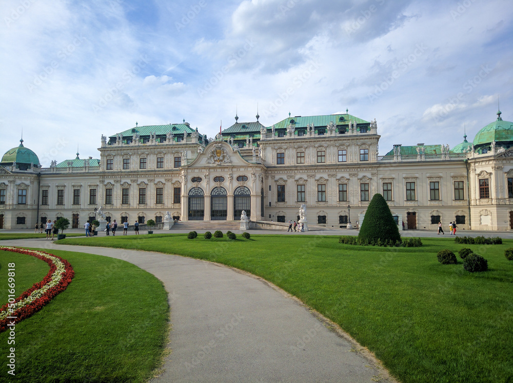 Vienna, Austria - August 15, 2019: View of the Belvedere Palace in Vienna, built in the Baroque style against the blue sky and clouds. People walk along the green lawns