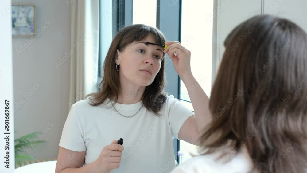 Portrait of a young woman who applies a transparent gel on her eyebrows in front of mirror. Portrait of a young woman who applies a transparent gel on her eyebrows in front of mirror.