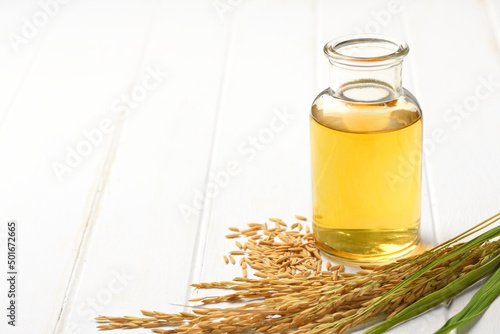 Rice bran oil with paddy rice and rice ears on white wood.