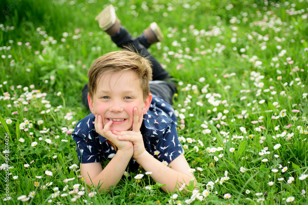 Happy child lying on green grass with daisy flowers. Smiling boy having fun outdoor in garden. Environmental, ecology and environment concept. Happy child lying on green grass with daisy flowers. Smiling boy having fun outdoor in garden. Environmental, ecology and environment concept.