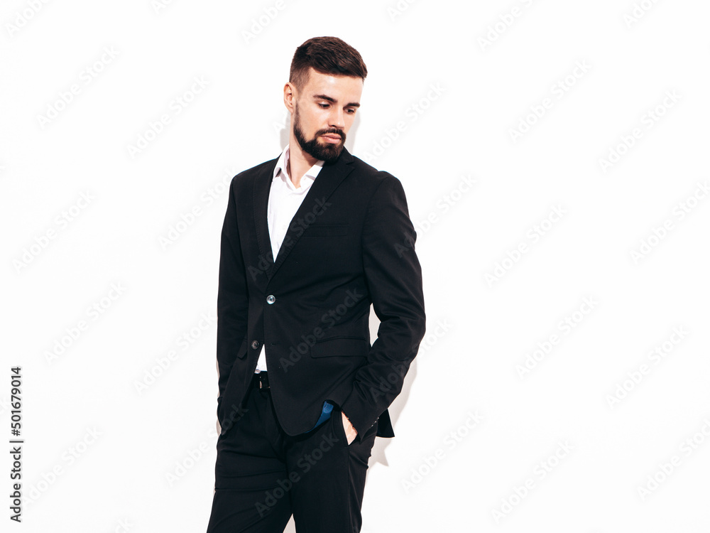 Portrait of handsome confident stylish hipster lambersexual model. Sexy modern man dressed in elegant black suit. Fashion male posing in studio near white wall. Isolated Portrait of handsome confident stylish hipster lambersexual model. Sexy modern man dressed in elegant black suit. Fashion male posing in studio near white wall. Isolated