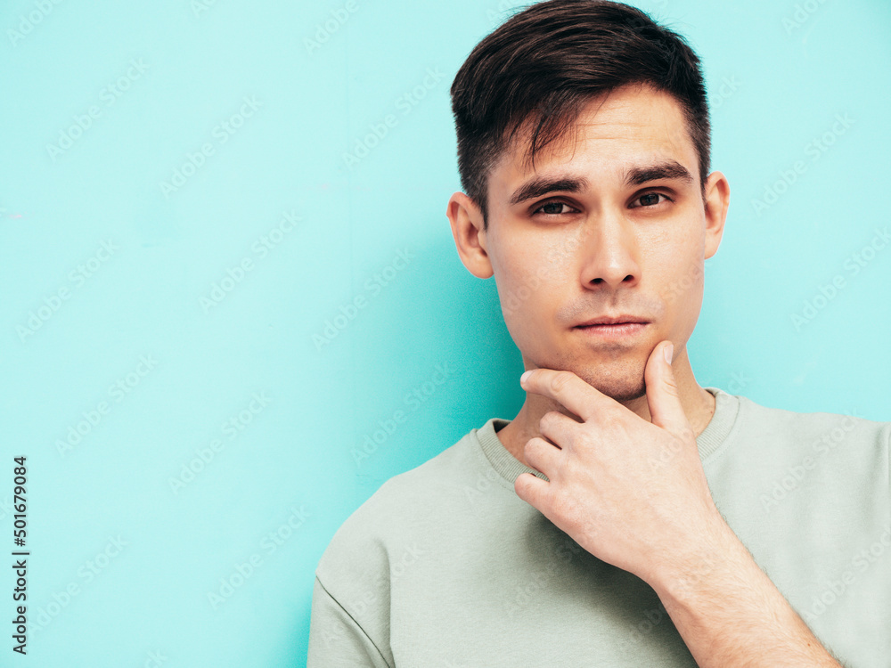 Portrait of handsome smiling stylish hipster lambersexual model.Man dressed in T-shirt and jeans. Fashion male isolated in studio. Posing near blue wall. Cheerful and happy. Touching his chin Portrait of handsome smiling stylish hipster lambersexual model.Man dressed in T-shirt and jeans. Fashion male isolated in studio. Posing near blue wall. Cheerful and happy. Touching his chin