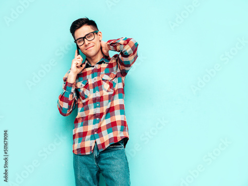 Handsome smiling model.Sexy stylish man talking at smartphone. Fashion hipster male posing near blue wall in studio. Holding phone. With cellphone. Isolated