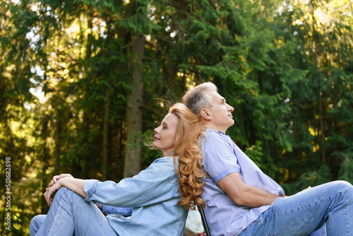 Portrait handsome mature man woman couple sitting back each other rest supporting each other, background summer green park in casual clothes caucasian pensioners relax in nature