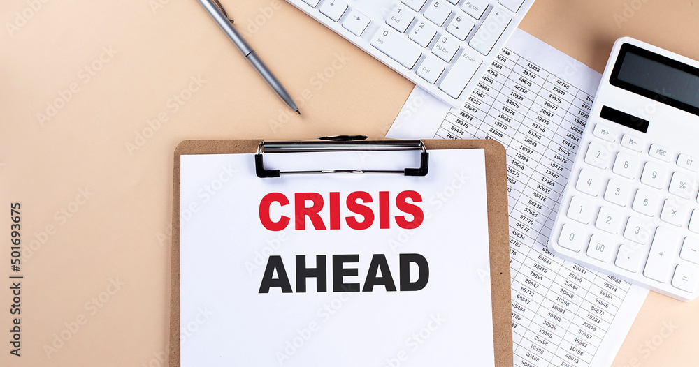 clipboard with white blank paper text CRISIS AHEAD , keyboard calculator and chart, top view. business concept. clipboard with white blank paper text CRISIS AHEAD , keyboard calculator and chart, top view. business concept.