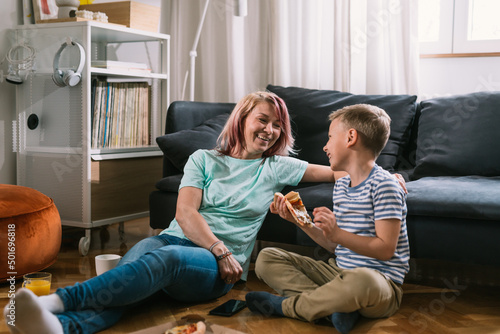 single mother and son enjoying time together at home, talking and eating pizza
