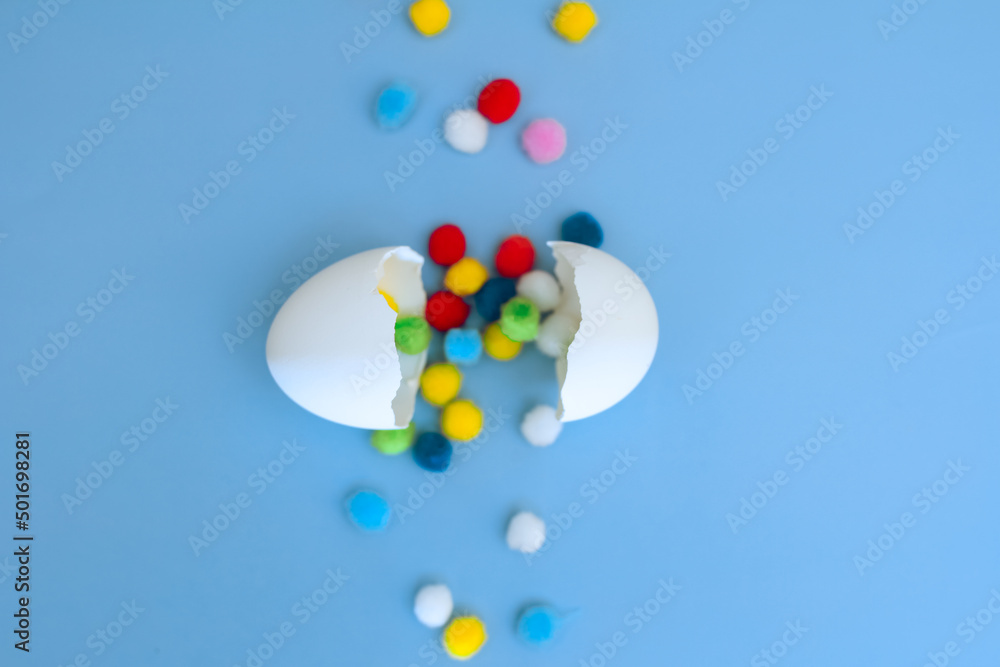 Eggshell and a path of multi-colored pompoms on a blue background, focus on the shell