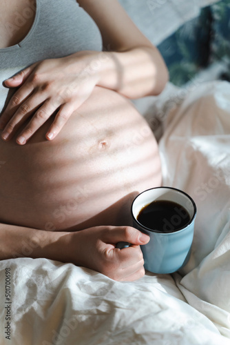 A pregnant woman holds a cup of coffee in her hands. Caffeine safety, myths about coffee during pregnancy concept 