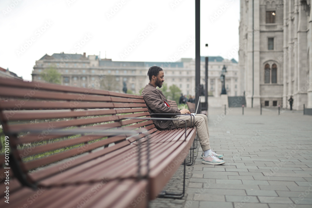 © olly - young man sitting on a bench uses a computer