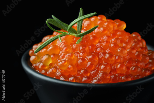 Bowl with delicious red caviar and rosemary on black background, closeup