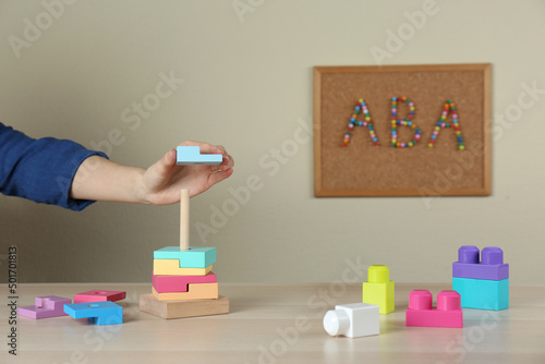 Child playing with toy pyramid at wooden table indoors, closeup. ABA therapy concept