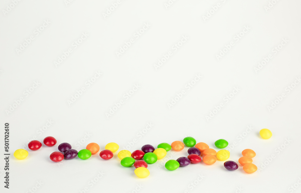 Multicolored round candies scattered on a white table with copy space. Beautiful sweets. Multicolored round candies scattered on a white table with copy space. Beautiful sweets.