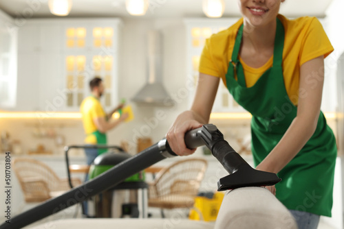 Professional janitor in uniform vacuuming sofa indoors, closeup. Space for text
