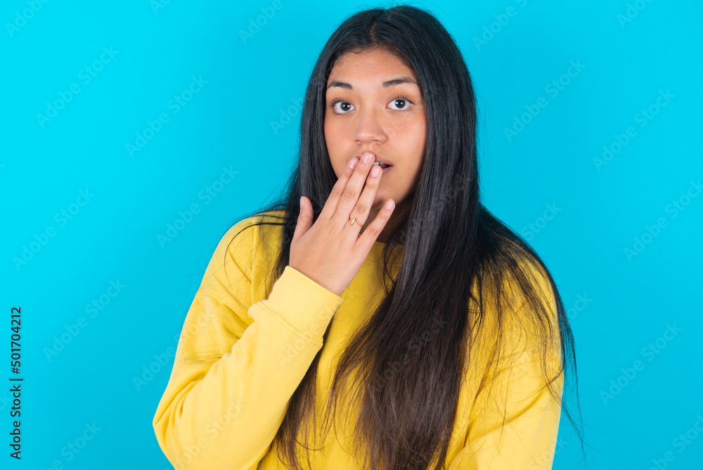 Oh! I think I said it! Close up portrait young latin woman wearing yellow sweater over blue background cover open mouth by hand palm, look at camera with big eyes. Oh! I think I said it! Close up portrait young latin woman wearing yellow sweater over blue background cover open mouth by hand palm, look at camera with big eyes.