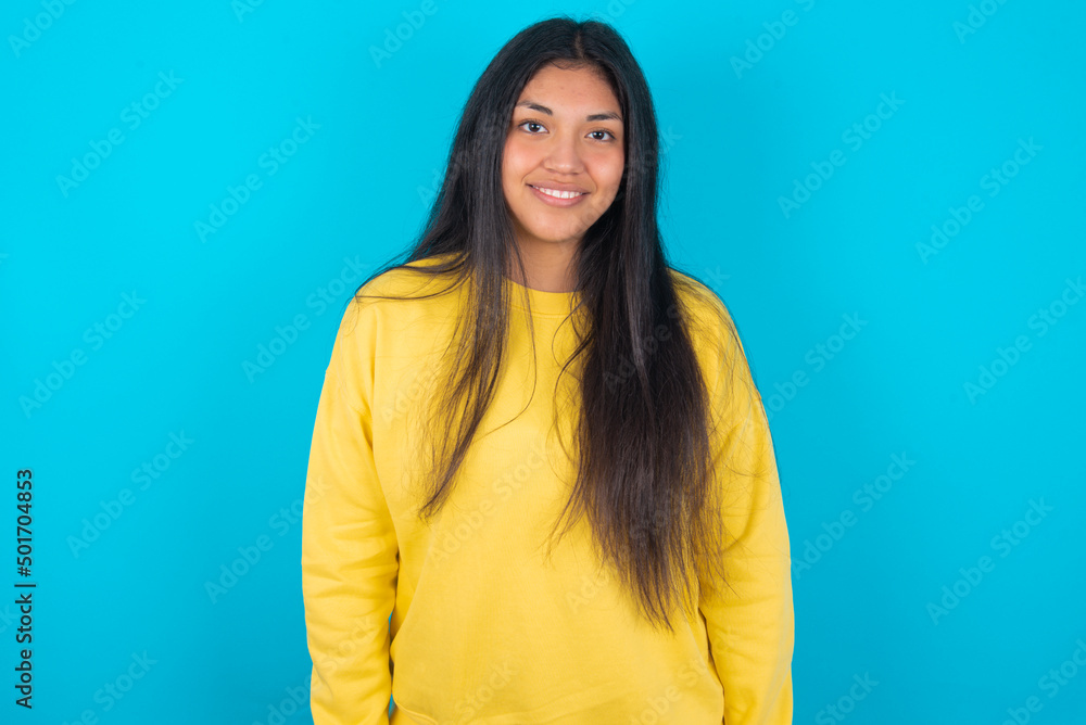 young latin woman wearing yellow sweater over blue background with nice beaming smile pleased expression. Positive emotions concept young latin woman wearing yellow sweater over blue background with nice beaming smile pleased expression. Positive emotions concept