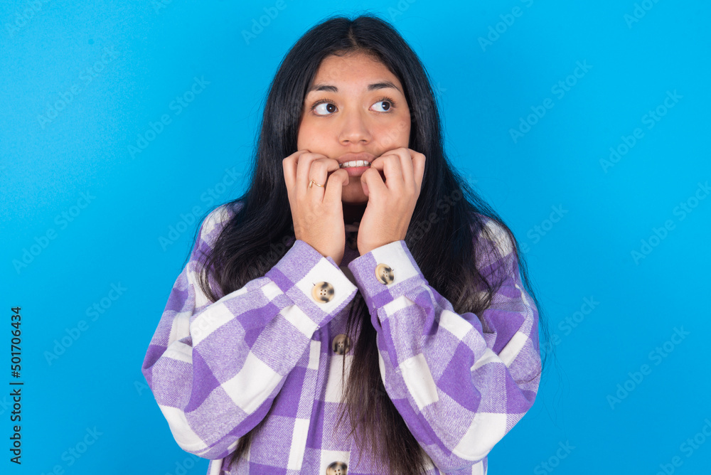 Terrified young latin woman wearing plaid shirt over blue background looks empty space home alone moonless night Terrified young latin woman wearing plaid shirt over blue background looks empty space home alone moonless night