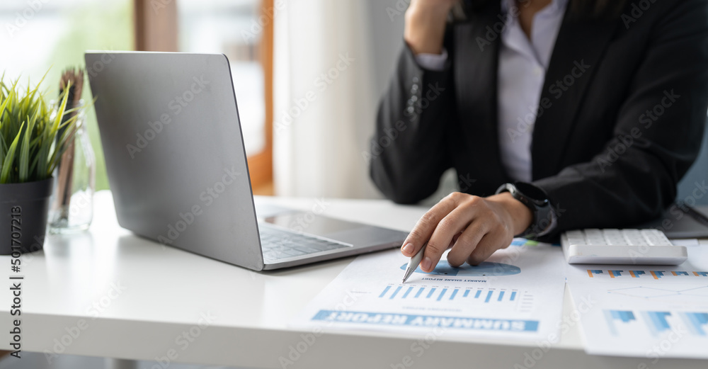 Business or bookkeeper woman pen pointing turnover with graph chart report and use laptop computer for analysis data Business or bookkeeper woman pen pointing turnover with graph chart report and use laptop computer for analysis data