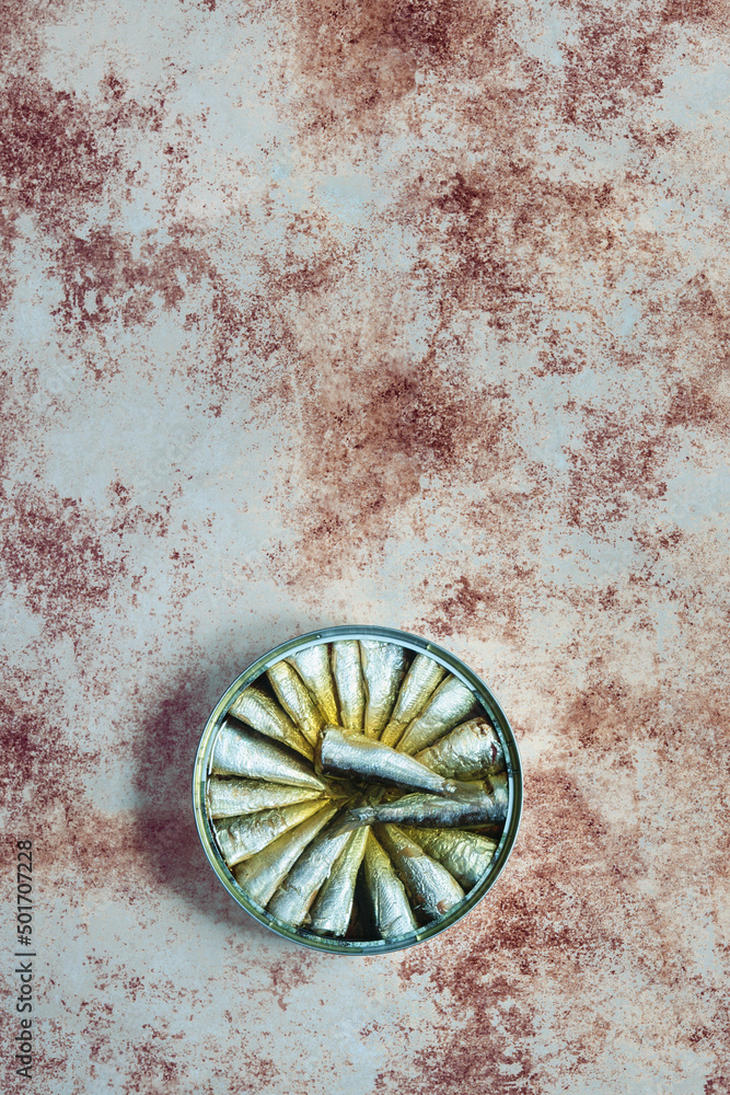 Overhead view of a large round sardine tin on a weathered and painted textured background. Food storage and fish.