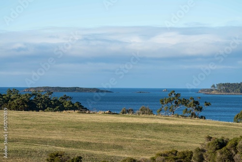 southern tasmania coastline with mountains, looking at bruny island with storm clouds and rain over the ocean, flying above a beach town and cattle, cow farm, in australia