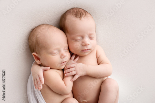 Tiny newborn twins boys in white cocoons on a white background. A newborn twin sleeps next to his brother. Newborn two twins boys hugging each other.Professional studio photography