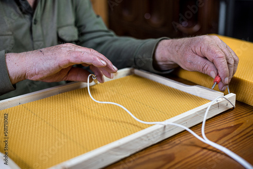 hands of old beekeeper are inserting of beeswax base into the bee frame. Heating the wire with an electrical resistor. photo