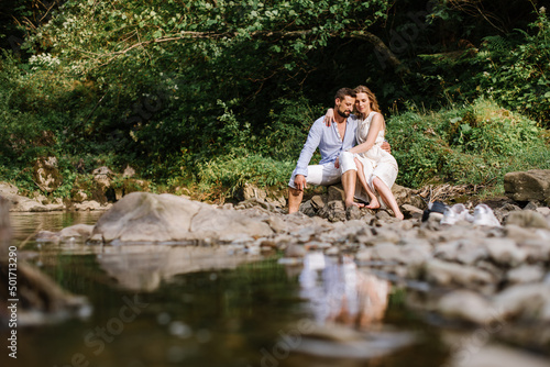 Loving couple sitting on the rocks by the river in the national park on a summer day