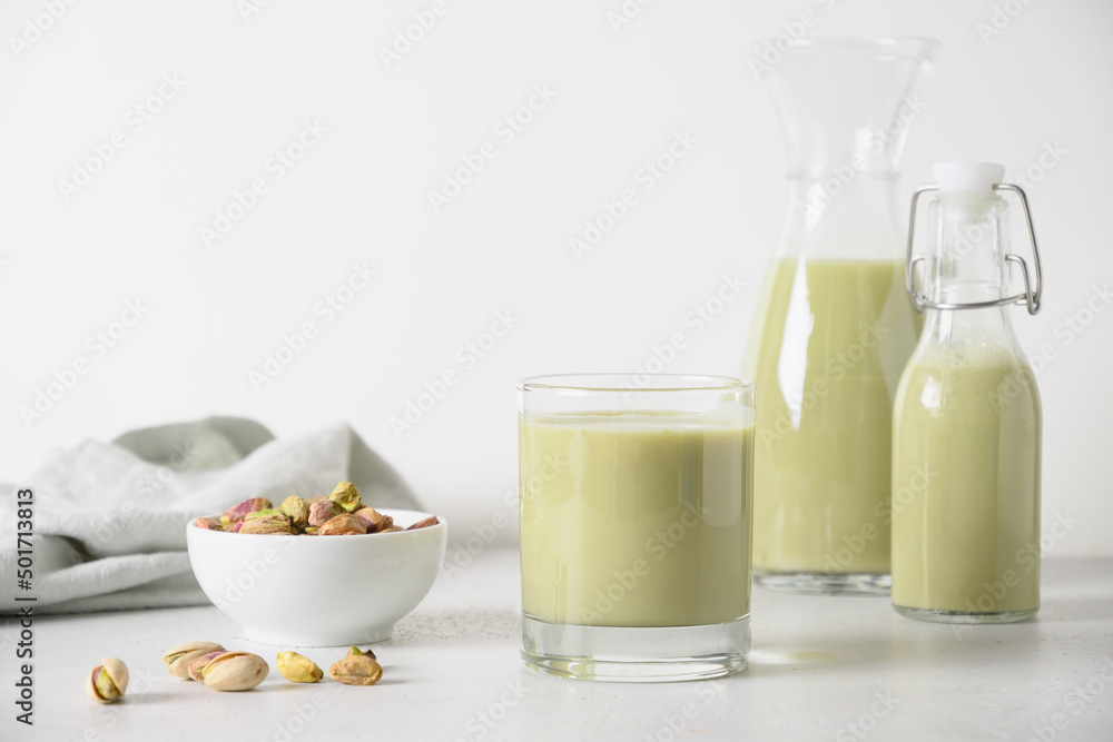 Pistachio milk in glasses and pistachios in glass jar on white kitchen background. Vegan nutty plant based milk. Vertical. Pistachio milk in glasses and pistachios in glass jar on white kitchen background. Vegan nutty plant based milk. Vertical.