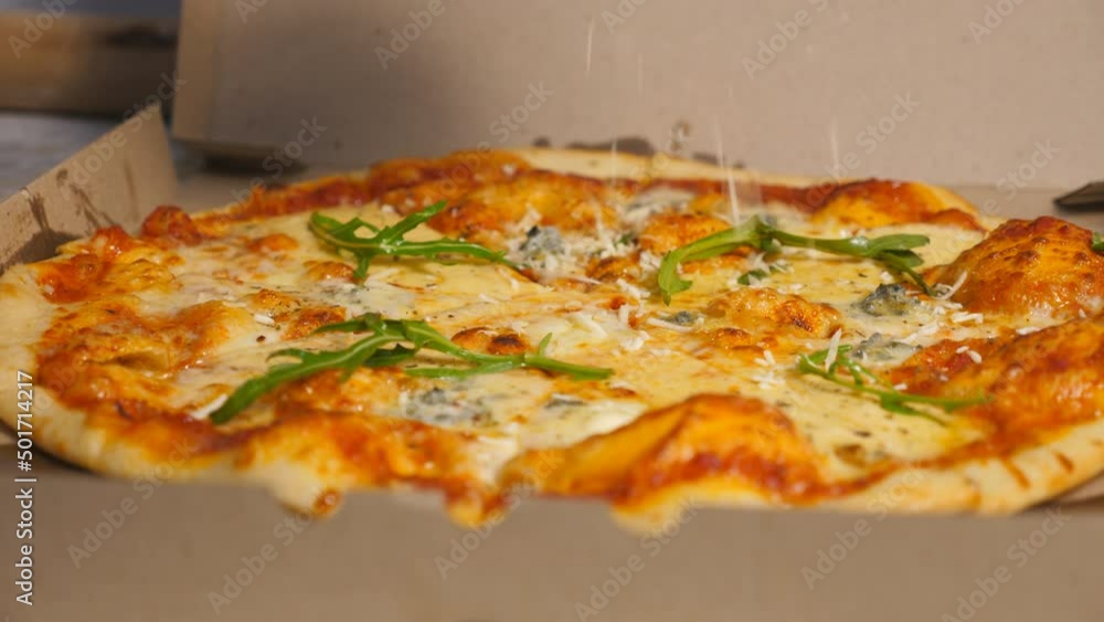 Male hand of chef in glove finishing tasty vegetarian pizza with a sprinkles grated parmesan at cuisine restaurant. Delicious baked dish in a carton box at kitchen pizzeria. Close up Slow motion Male hand of chef in glove finishing tasty vegetarian pizza with a sprinkles grated parmesan at cuisine restaurant. Delicious baked dish in a carton box at kitchen pizzeria. Close up Slow motion