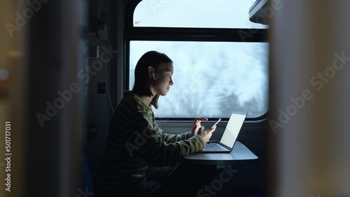 Beautiful female tourist rides with a laptop on the train, works and uses a smartphone with a serious face.